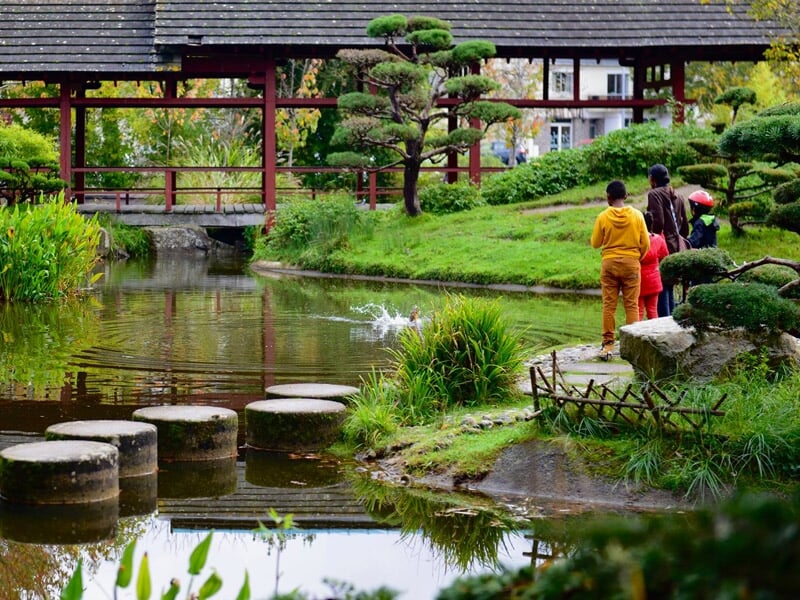 Famille se promenant dans un jardin japonais avec un étang et un pont en bois sous un ciel nuageux.