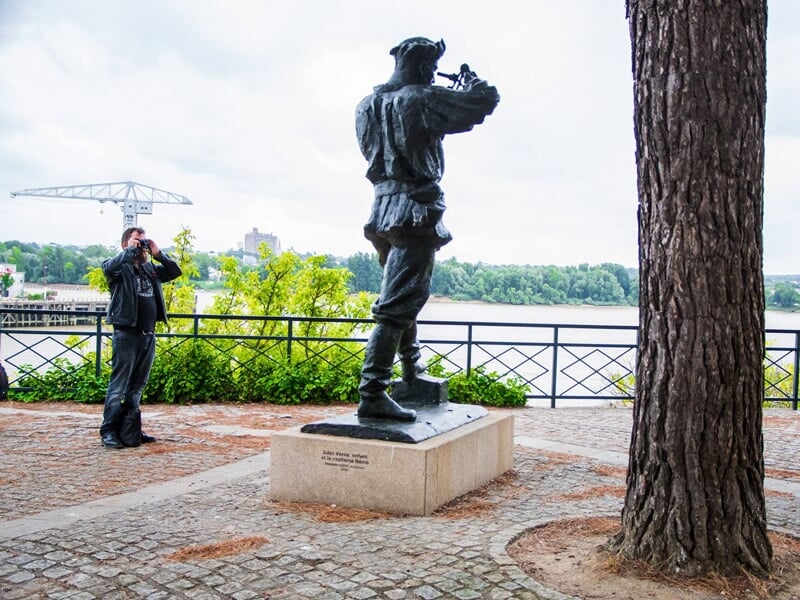 Homme prenant une photo d'une statue en bronze près d'un plan d'eau dans un parc urbain.