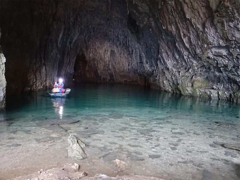 Personnes en bateau dans une grotte avec eau claire et parois rocheuses sombres.