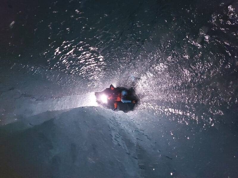 Personne descend en rappel dans une crevasse glacée avec équipement de spéléologie sur glace.