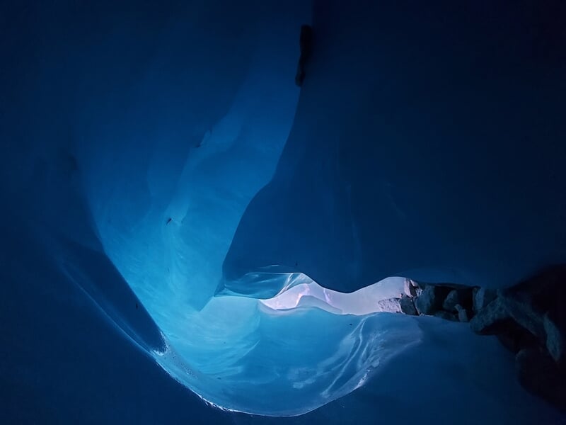 Vue intérieure d'une grotte de glace bleue avec lumière naturelle filtrant à travers la glace.