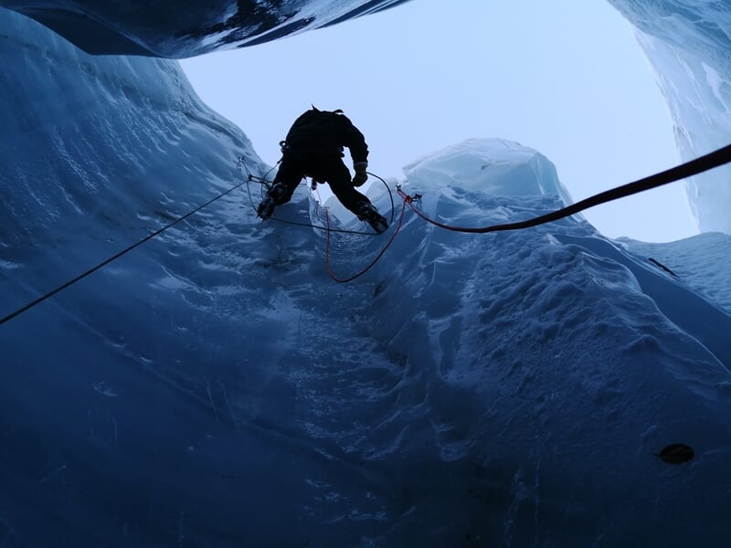 Spéléologue descend en rappel dans une crevasse glacée étroite avec équipement spécialisé.