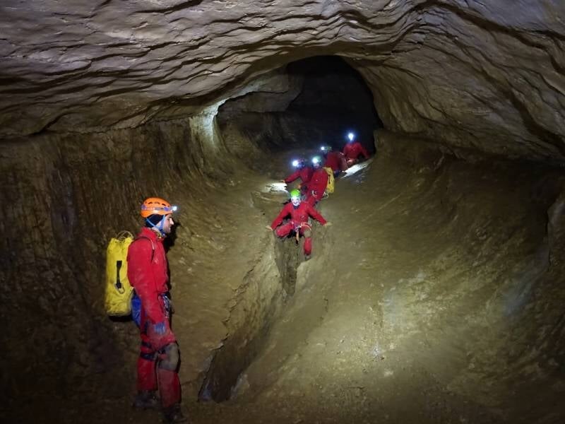 Groupe de spéléologues équipés de lampes frontales progressant dans un tunnel étroit de grotte.