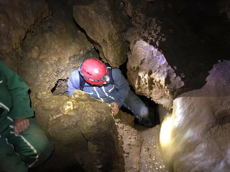 Personne avec casque rouge explorant une grotte étroite et rocheuse lors d'une activité d'escape game aventure.
