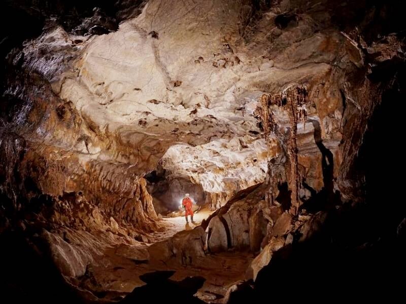 Spéléologue seul avec lampe frontale dans une vaste cavité rocheuse aux parois sculptées.