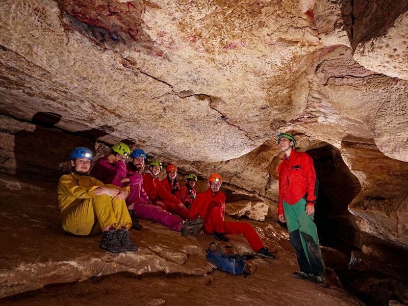 Groupe de spéléologues assis dans une cavité souterraine, équipés de casques et combinaisons colorées.