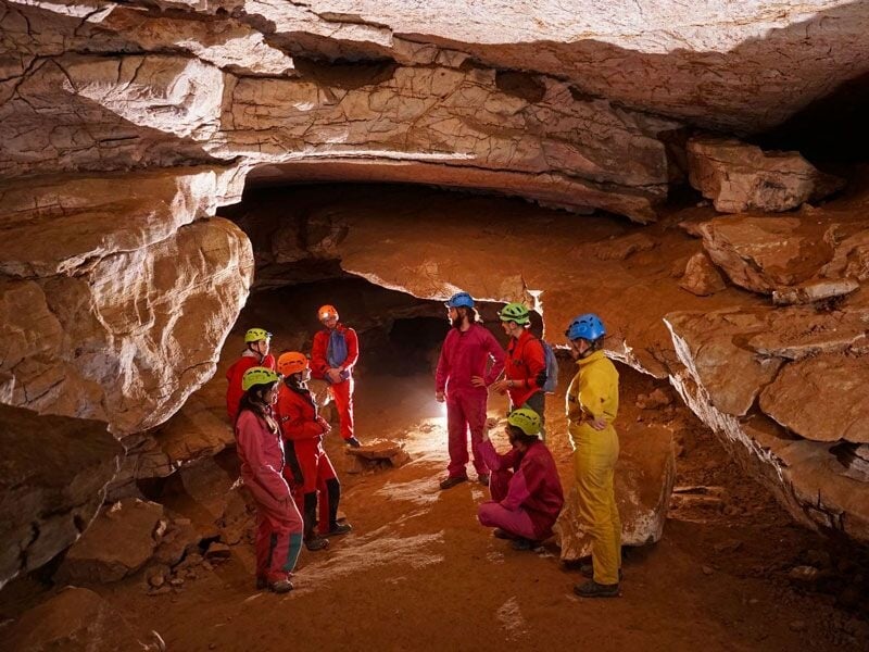 Spéléologues en cercle dans une grande salle souterraine aux parois rocheuses, discutant ou se reposant.