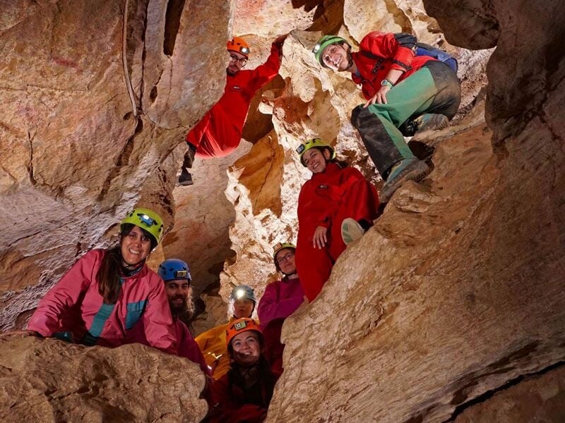Groupe de spéléologues souriants posant dans une cavité rocheuse étroite, éclairés par leurs lampes frontales.