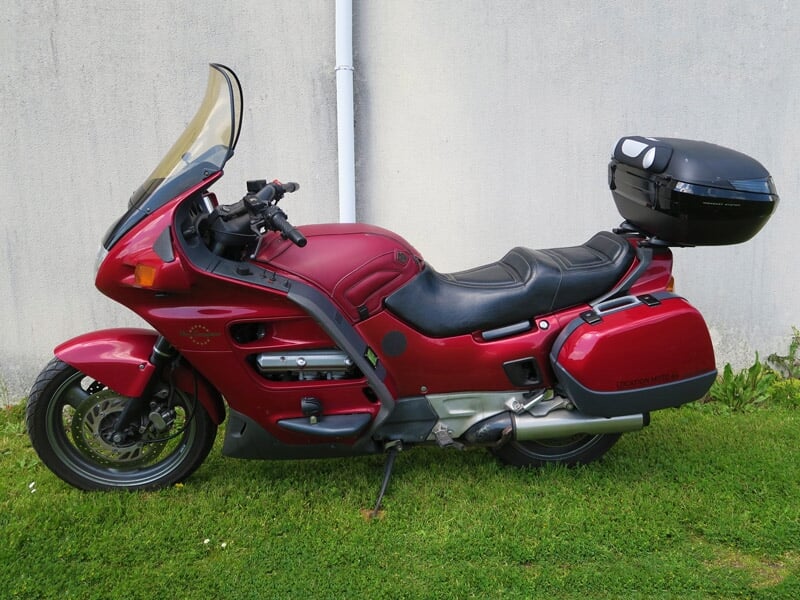 Moto rouge garée sur une pelouse verte devant un mur gris, prête pour une randonnée à Corcoué-sur-Logne.