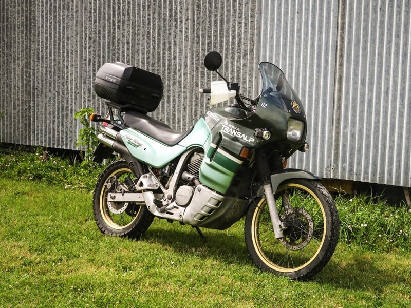 Moto verte et noire stationnée sur l'herbe devant un bâtiment métallique, équipée pour un voyage aventure.