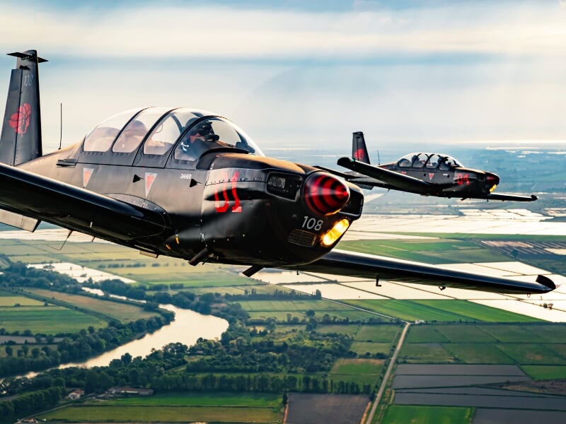 Deux avions d'entraînement militaires en vol en formation rapprochée au-dessus d'un paysage de campagne et de rivières
