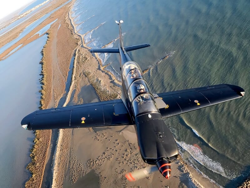 Vue aérienne d'un avion d'entraînement militaire volant à basse altitude au-dessus d'une plage et de la mer