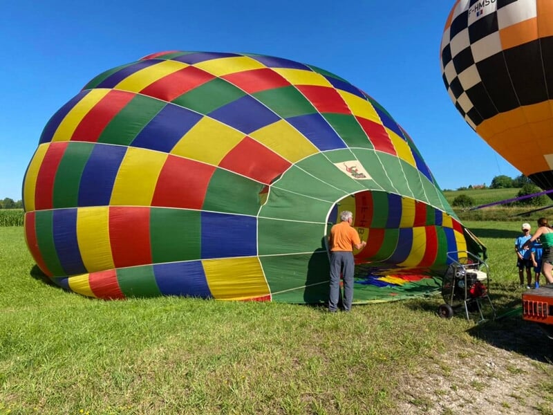 Montgolfière colorée en cours de gonflage sur un champ vert avec des personnes autour par beau temps.