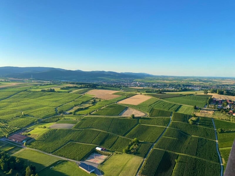 Paysage agricole vu du ciel avec des champs verts et des collines à l'horizon sous un ciel bleu clair.