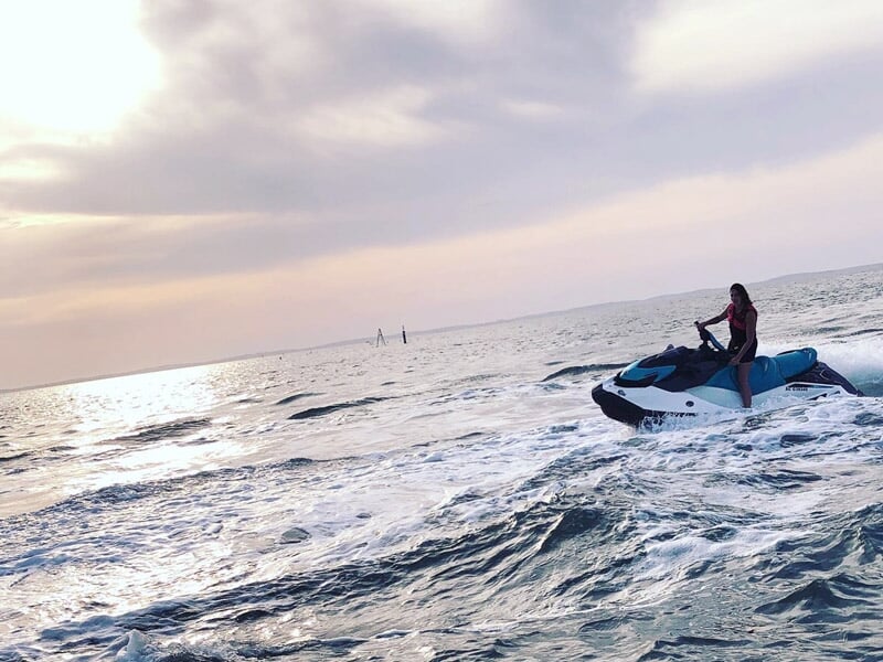 Personne sur un jetski bleu et blanc naviguant sur une mer agitée au coucher du soleil à Arcachon.