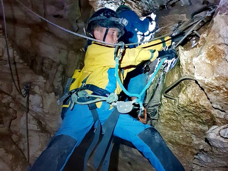 Personne équipée d'un casque et harnais progressant dans une grotte rocheuse lors d'une sortie spéléologie.