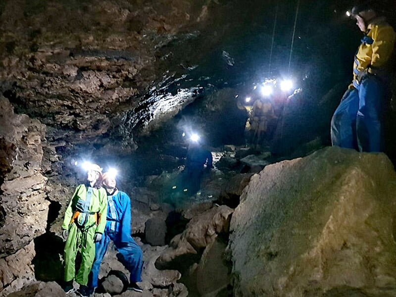 Groupe de spéléologues avec lampes frontales explorant une vaste cavité souterraine rocheuse.
