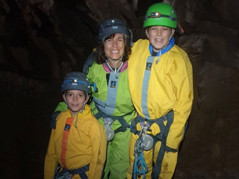 Trois personnes en tenue de spéléologie posant ensemble dans une grotte sombre et rocheuse.