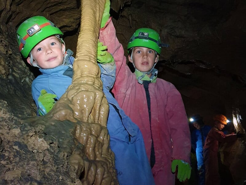 Deux enfants en combinaison colorée explorant une formation rocheuse dans une cavité souterraine.