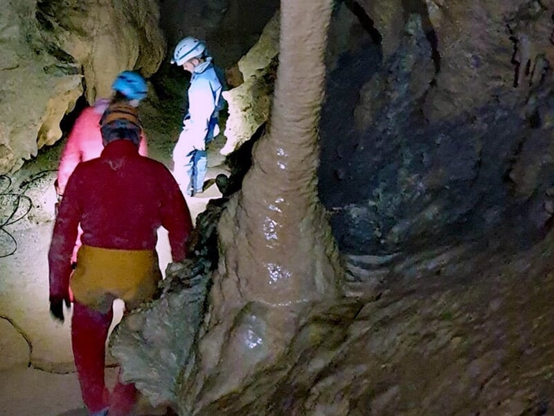 Groupe de spéléologues progressant dans une grotte avec des casques et lampes frontales allumées.