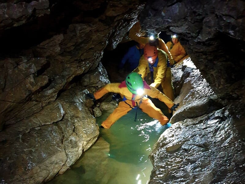 Groupe de spéléologues explorant une grande salle rocheuse dans une grotte avec lampes frontales.