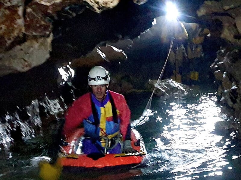 Spéléologues traversant une rivière souterraine dans une grotte, certains sur un radeau gonflable.
