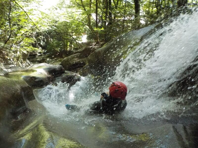 Personne glissant dans un toboggan naturel en eau vive entourée de rochers et de végétation dense en canyoning.