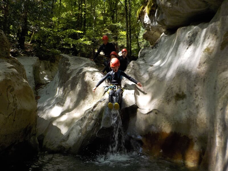 Groupe de personnes en casque rouge sautant dans une rivière encaissée lors d'une activité de canyoning en montagne.