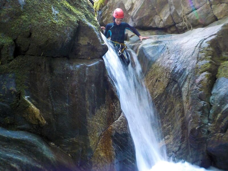 Descente en rappel d'une cascade dans un canyon rocheux avec un fort débit d'eau et une végétation en arrière-plan.