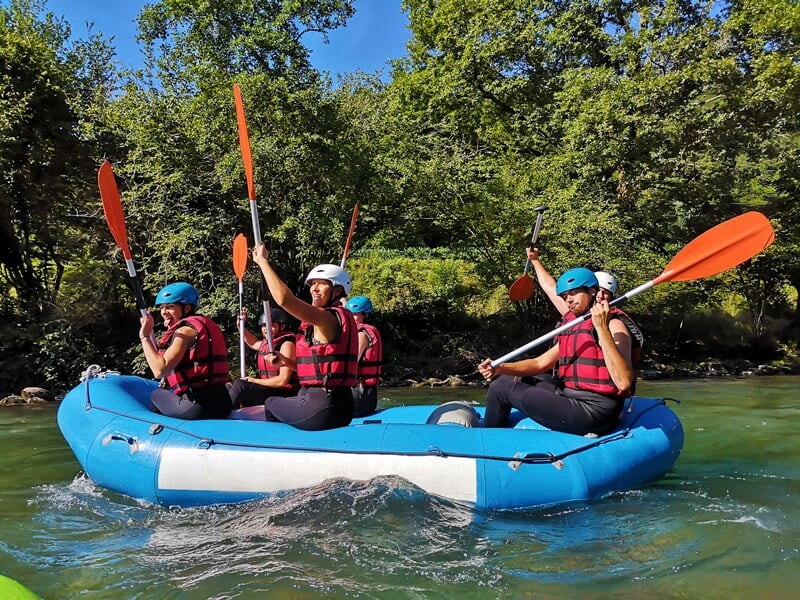 Quatre personnes pagayant ensemble dans un raft bleu sur une rivière entourée d'arbres verts.