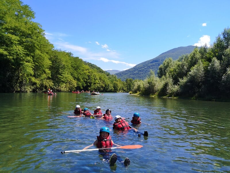Groupe de personnes flottant dans une rivière en tenue de rafting sous un ciel bleu et un paysage montagneux.