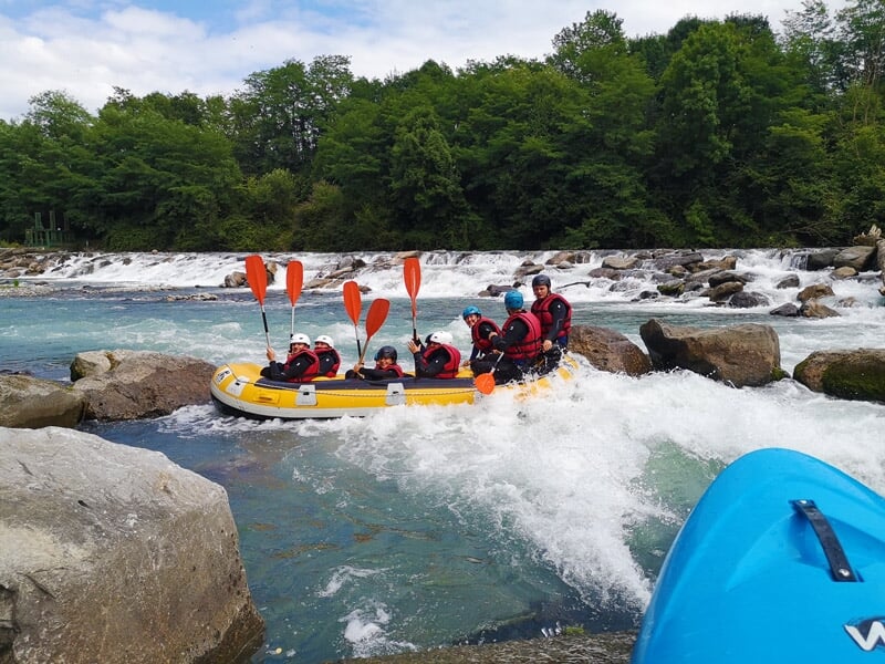 Groupe de personnes en raft jaune pagayant dans des rapides avec des rochers et de l'eau agitée.