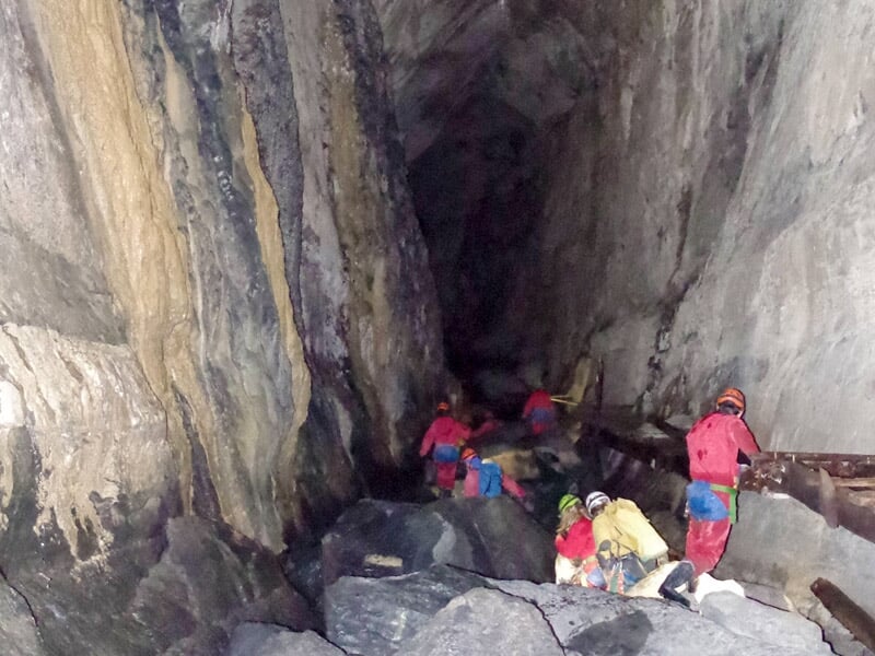 Groupe de spéléologues progressant dans une vaste galerie rocheuse humide, entourés de parois imposantes et sombres