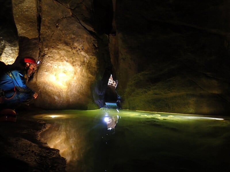 Spéléologue suspendu en rappel dans une grotte sombre avec équipement de sécurité et casque rouge.