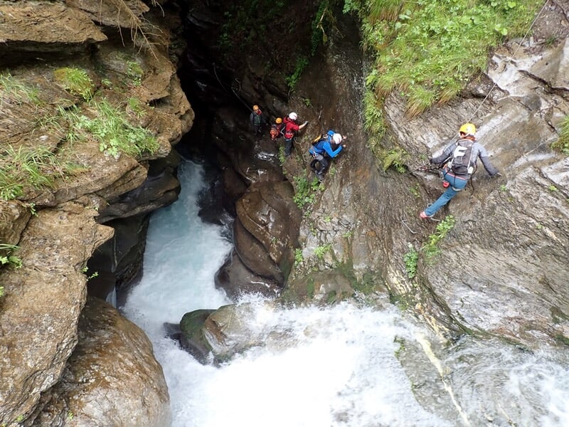Groupe de personnes en casque et harnais progressent sur un sentier aérien en via ferrata dans un paysage vert.