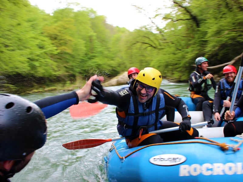 Groupe de personnes en raft bleu pagayant sur une rivière avec eau vive et rochers, ambiance sportive.