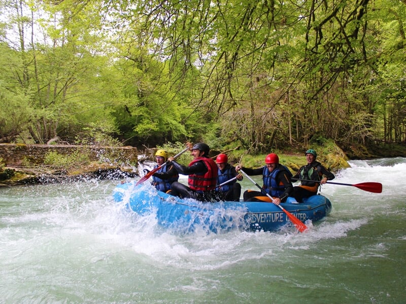 Rafting en rivière agitée avec plusieurs personnes en gilets de sauvetage et casques pagayant ensemble.