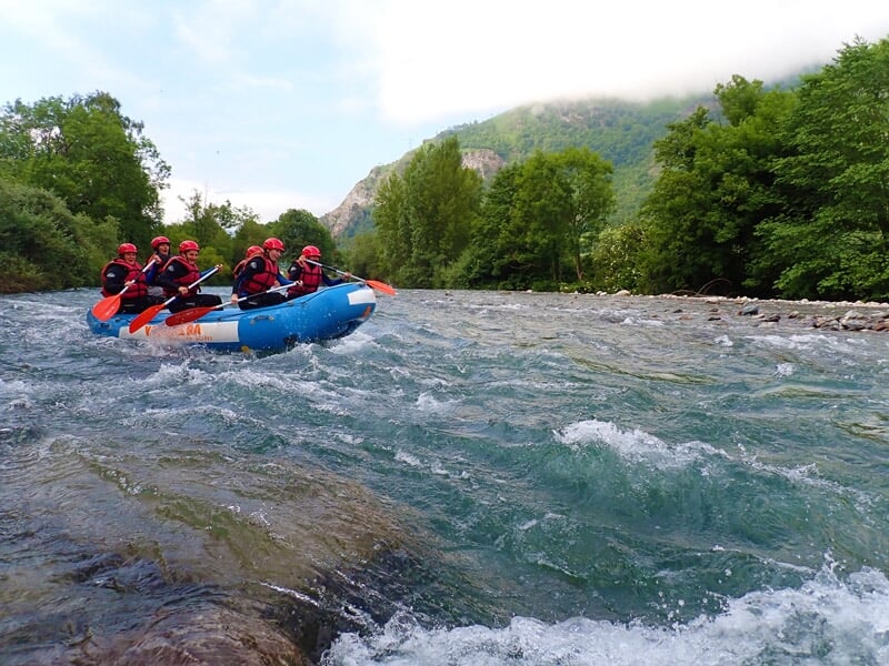 Groupe en raft bleu descend une rivière avec rapides, pagayant en coordination sous un ciel clair.
