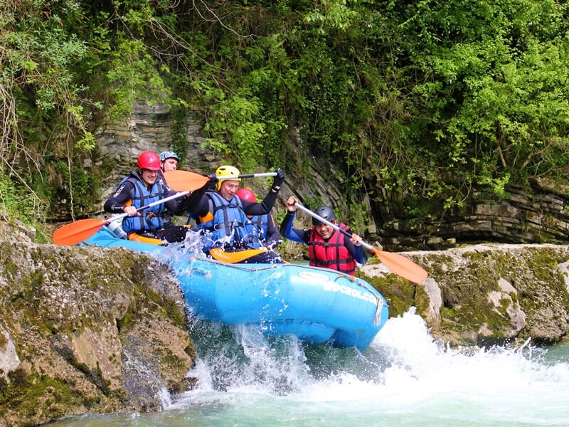 Rafting en rivière avec plusieurs personnes en gilets rouges et casques pagayant dans des rapides.