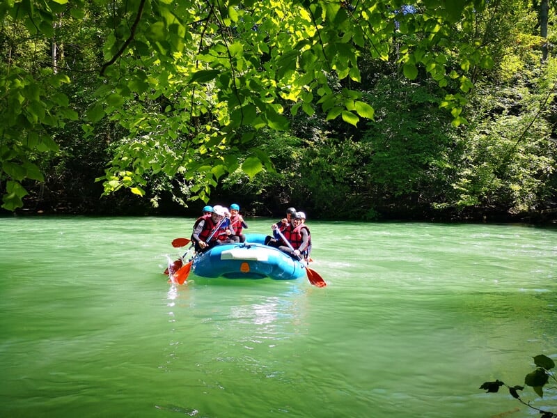 Groupe en raft bleu descend une rivière avec eau vive et rochers, pagayant avec énergie et coordination.