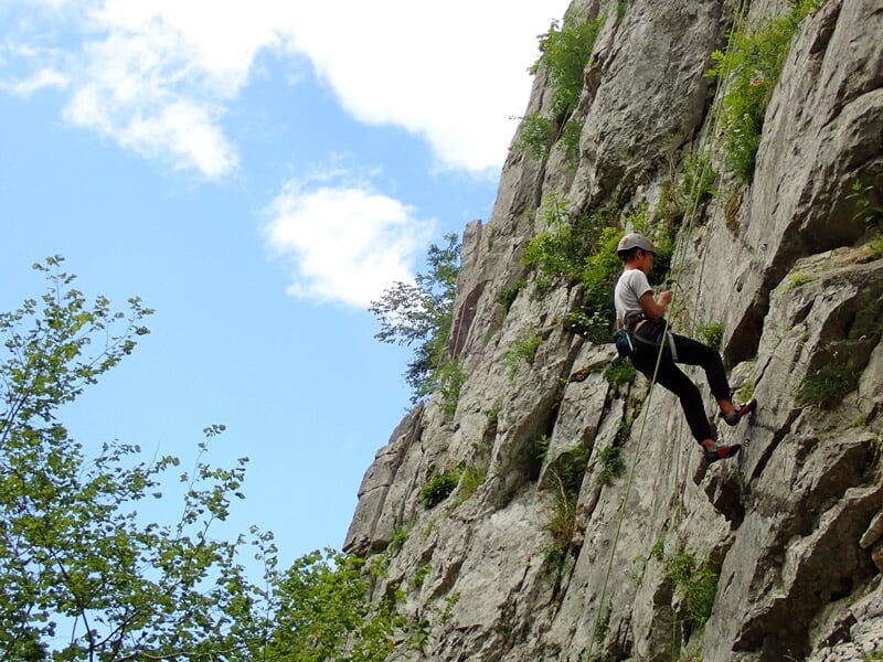 Personne en casque et harnais escalade une paroi rocheuse verticale dans un cadre naturel montagneux.