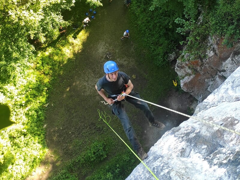 Escalade en extérieur avec plusieurs personnes en casque et harnais sur une falaise rocheuse.