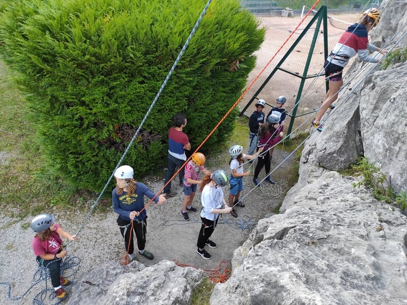 Personne en casque bleu et harnais descend en rappel une paroi rocheuse dans un environnement naturel.
