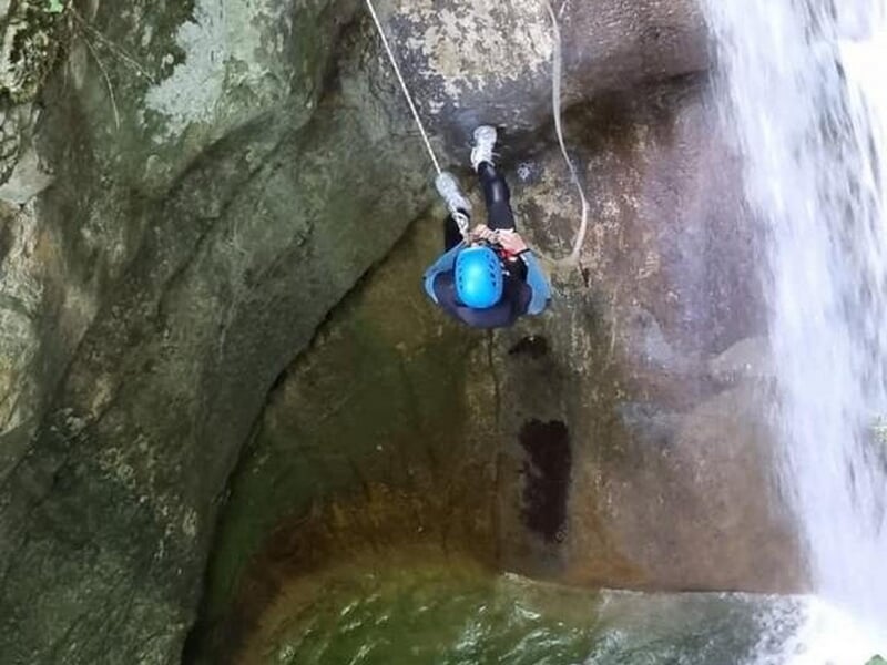 Personne en casque descend en rappel une cascade étroite dans un canyon rocheux avec eau en contrebas.