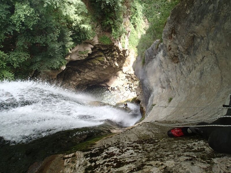 Vue plongeante sur une cascade puissante dans un canyon rocheux avec une personne en équipement d'escalade.