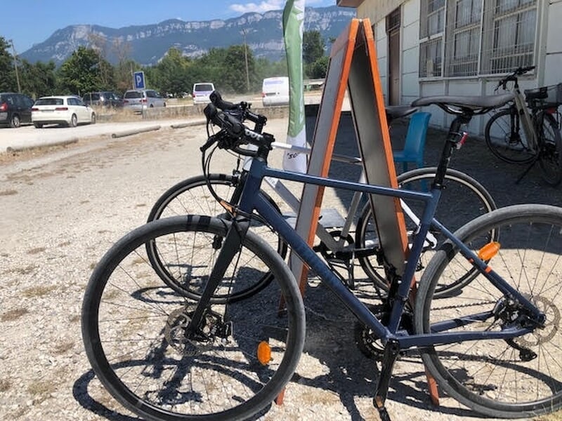 Vélo de montagne posé devant un panneau orange avec d'autres vélos et voitures en arrière-plan.