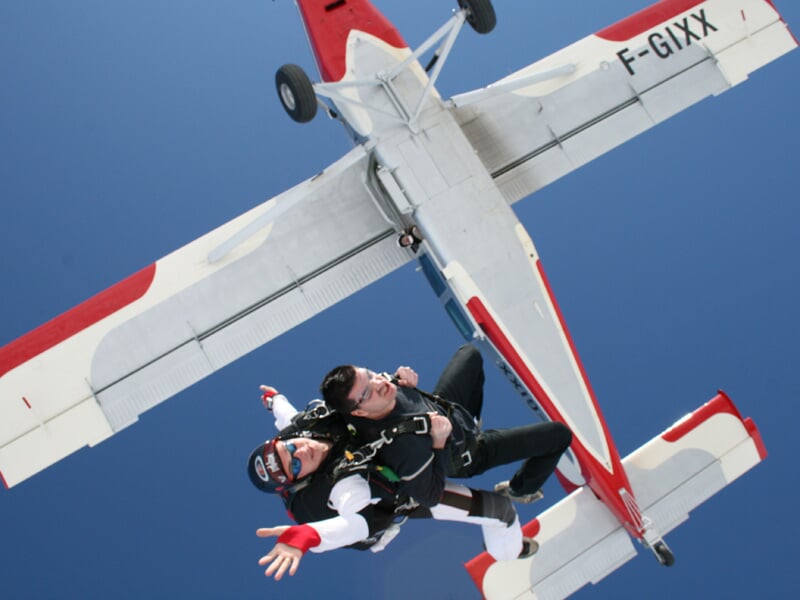 Un tandem de parachutistes vient de sauter d'un avion biplace blanc et rouge, immatriculé 