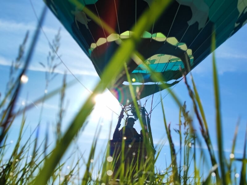Montgolfière colorée vue du sol avec herbe verte et soleil éclatant en arrière-plan.