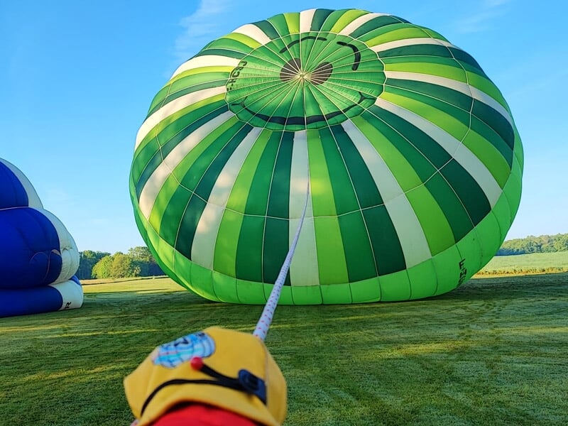 Montgolfière verte et blanche en train d'être gonflée sur un champ au lever du jour.