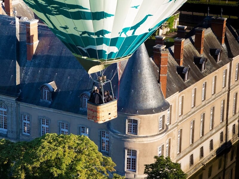 Montgolfière survolant un château ancien avec tours et toits en ardoise.